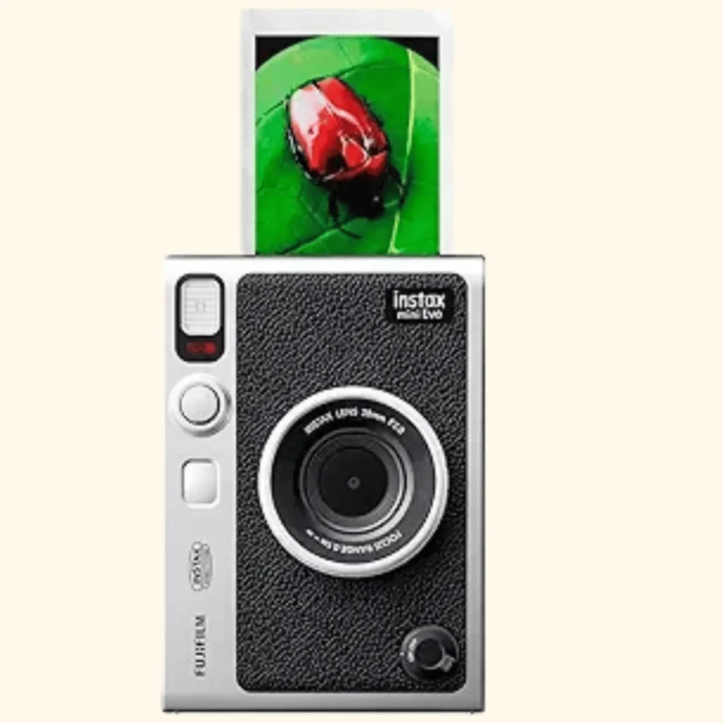 front-facing product shot of the Fujifilm Instax Mini EVO hybrid instant camera, featuring its classic silver and black leatherette retro design. A physical instant photo of a bright red beetle on a green leaf is shown emerging from the top of the camera's built-in printer slot.