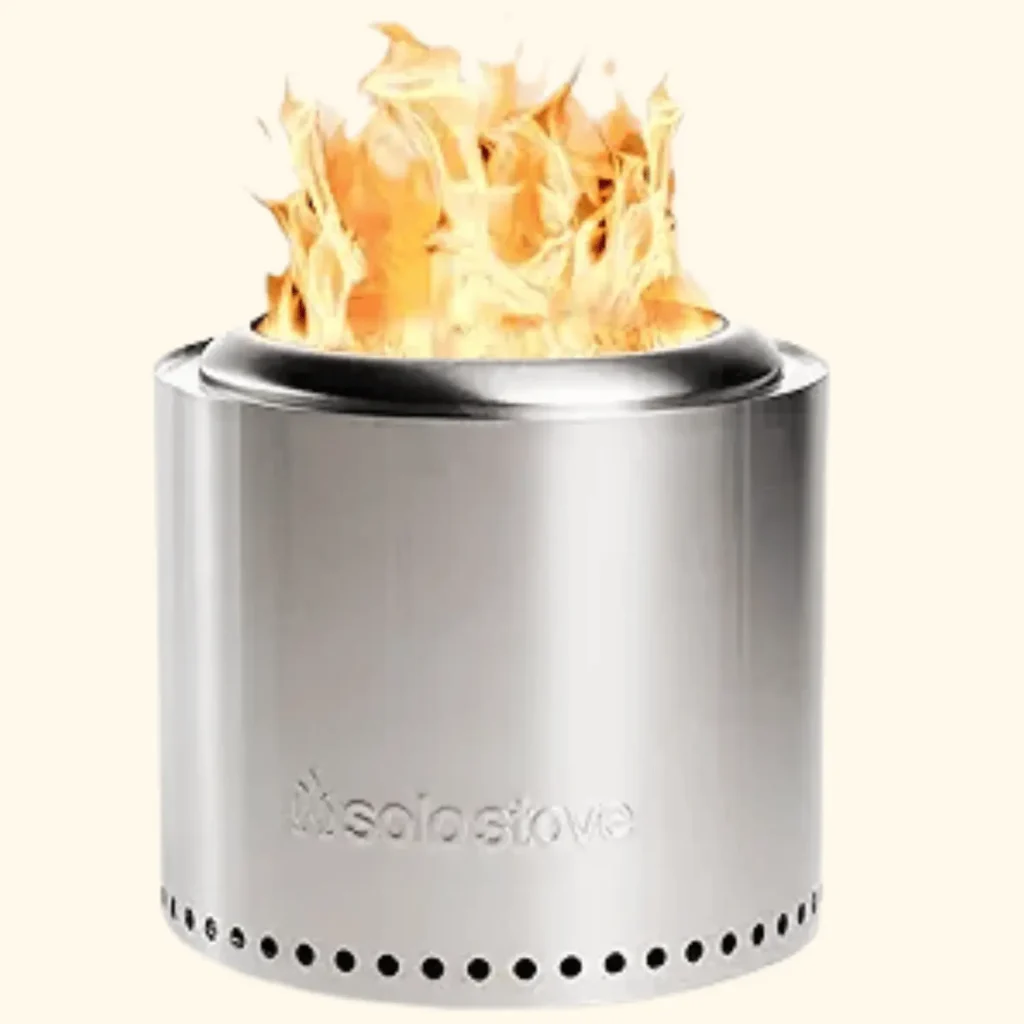 A product shot of the Solo Stove Ranger portable fire pit, featuring a sleek stainless steel cylindrical body with a series of precision-drilled ventilation holes around the base. The image shows the unit in operation with a smokeless bright orange flame rising from the top opening.