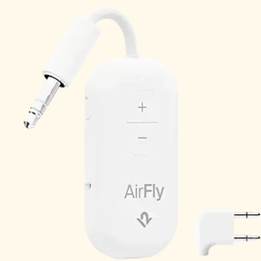 A product shot of the Twelve South AirFly Pro, a small, pill-shaped Bluetooth wireless transmitter in white. It features a single central button, a 3.5mm audio jack connector on a short integrated cable, and a protective cap, designed to connect wireless headphones to airplane entertainment systems.
